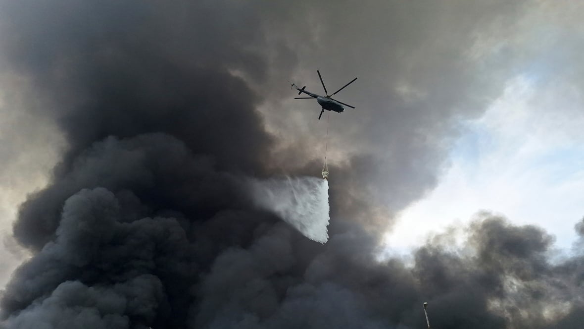 A helicopter flying amid black smoke drops water.